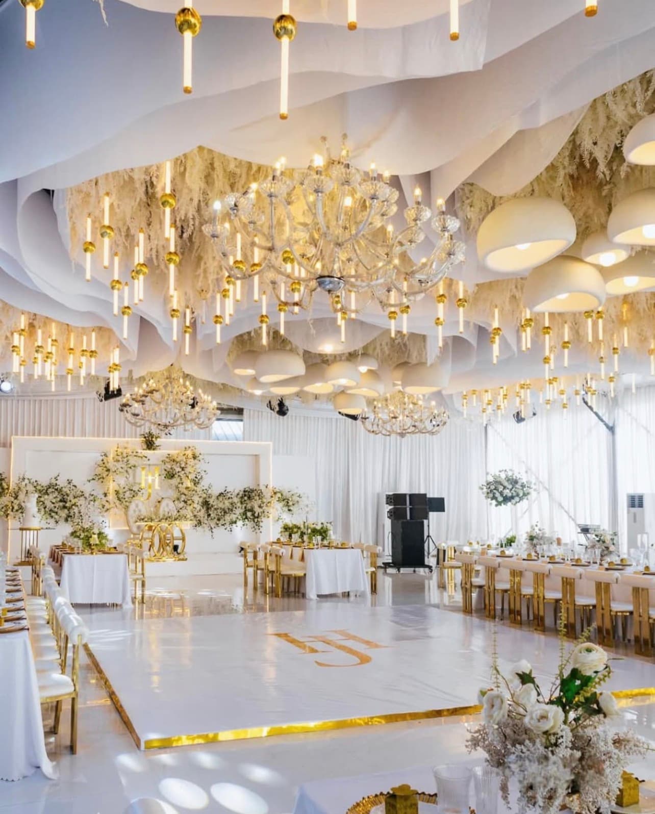 White and gold wedding reception with chandeliers, draped ceiling, and a monogrammed dance floor